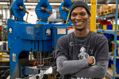 Corporate photography of a smiling male production line worker in front of his hydraulic press