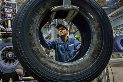 Operator handling a Michelin tire in preparation for a refurbishing process inside a truck maintenance facility