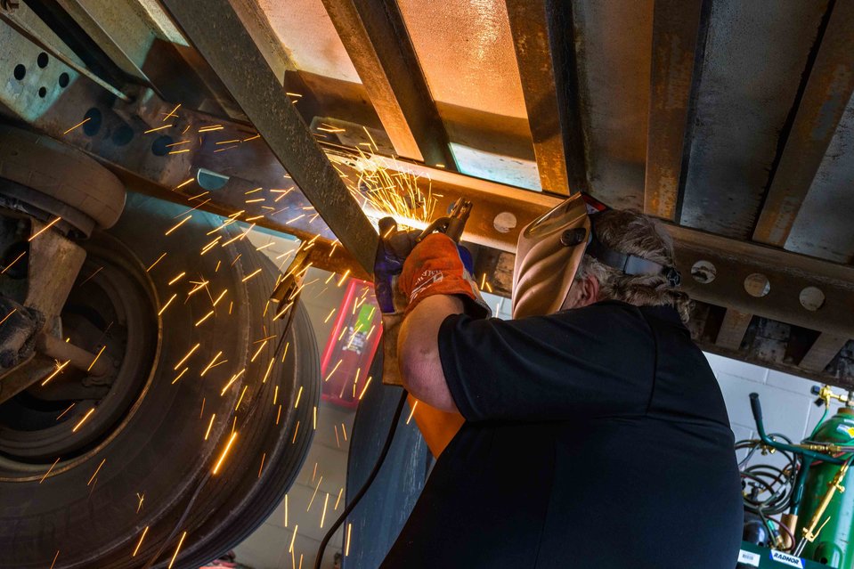 Worker in action underneath a truck trailer welding a steel part 