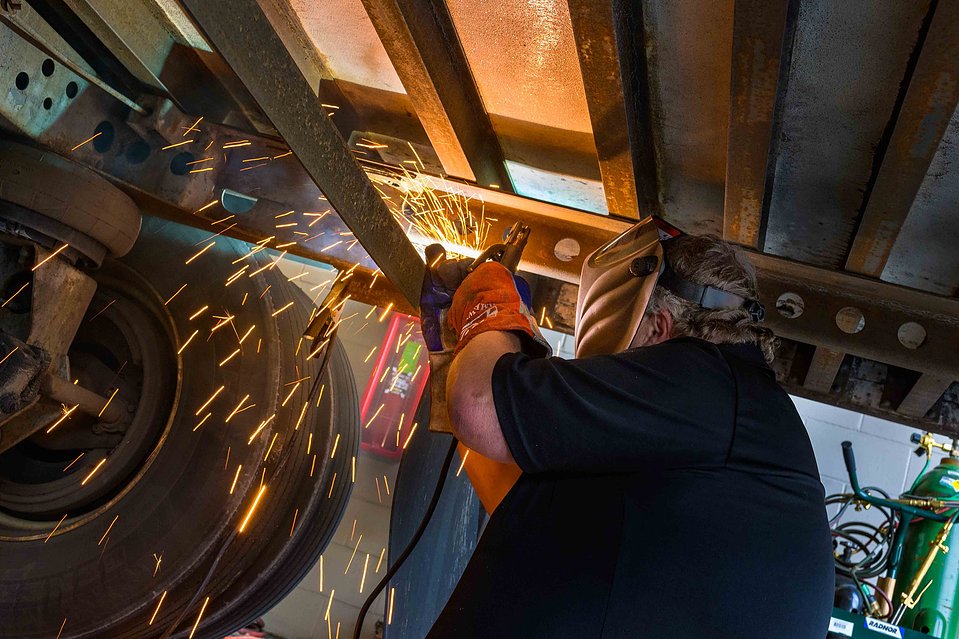 Worker in action underneath a truck trailer welding a steel part 