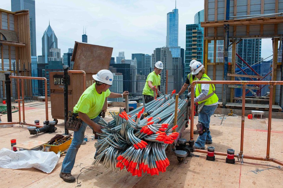 Construction crew handling materials on top of a skyscraper under construction