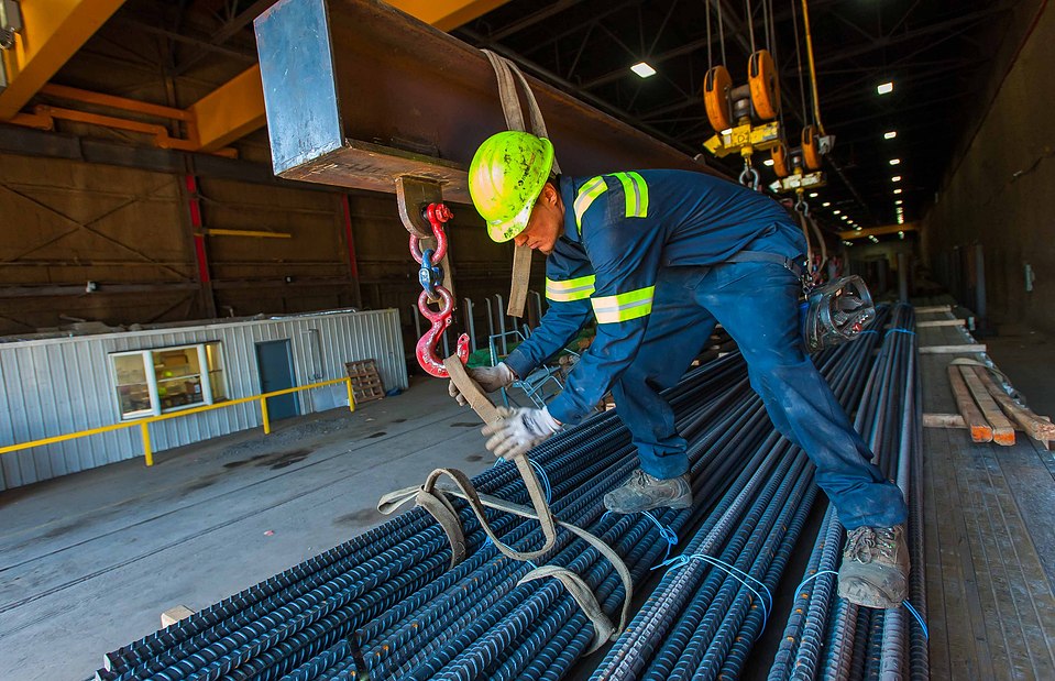 Worker of steel fabricator shipping department handling outbound freight on a truck flatbed trailer