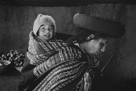 A mother carries a child on her back wearing the traditional Peruvian garb in the village of Ccor Ccor, Peru.