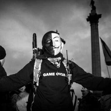 A masked demonstrator stands defiant in a Black Hoodie emblazoned 