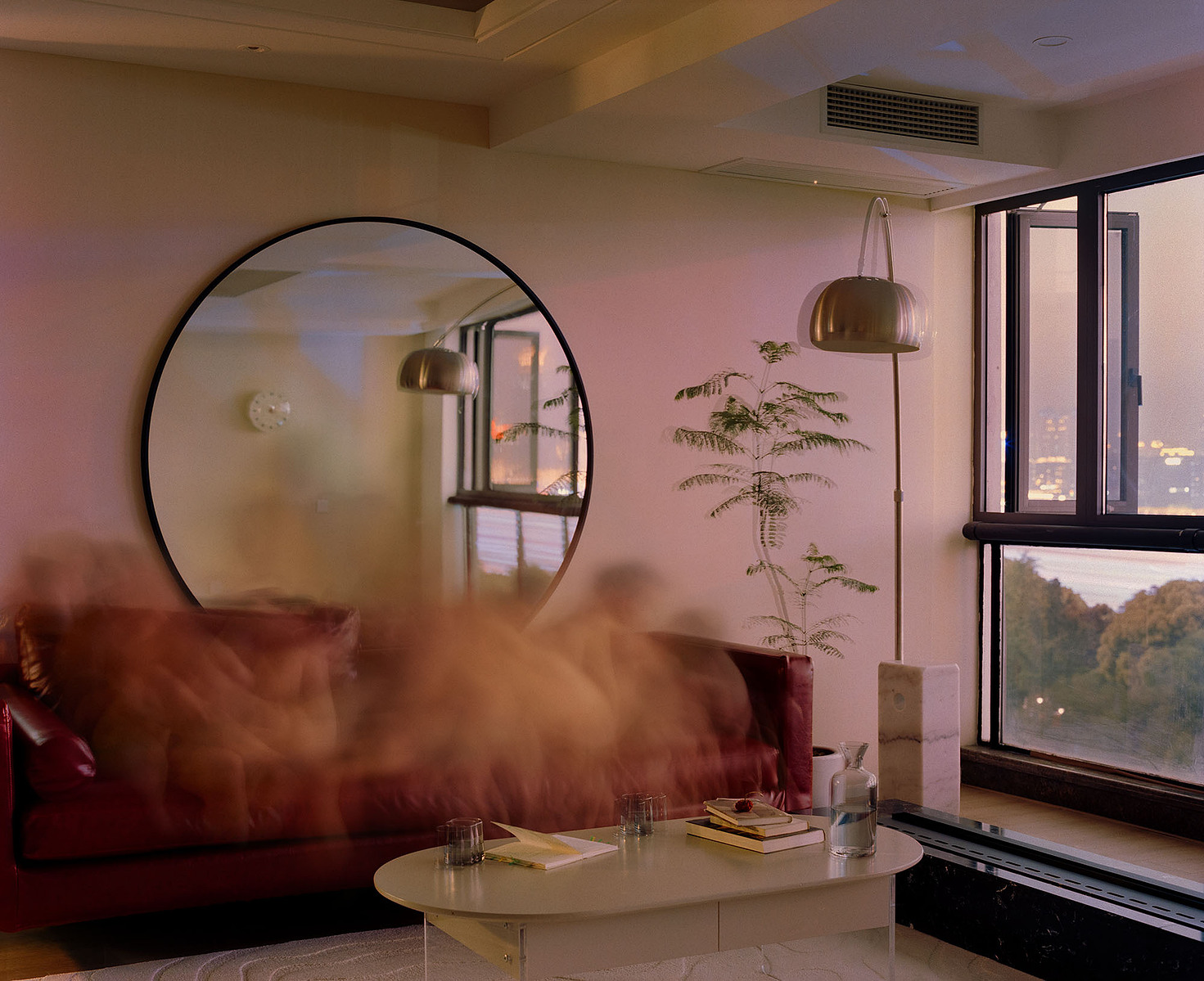 Blurred human figures on a blue bedsheet bed atop a round carpet, with purple tulips and a blue glass on the bedside table. In the background, a standing lamp, fan, closet with books and decor, an old Shanghai-style window, ceiling lamp, and wooden door.