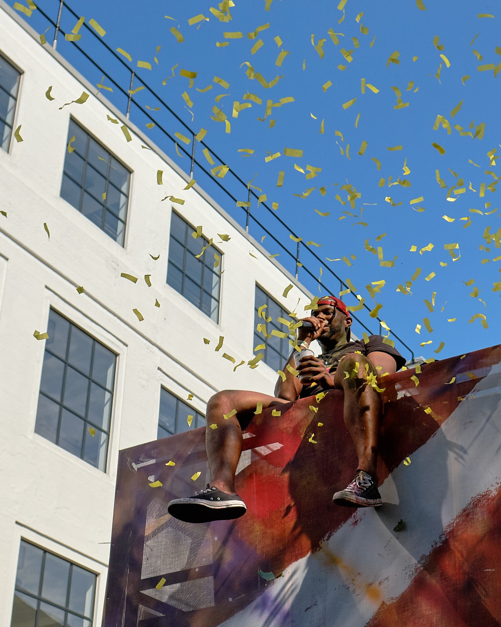 a man sits on top of a truck MC while confetti falls from the sunny sky. Notting Hill Carnival. London, UK.