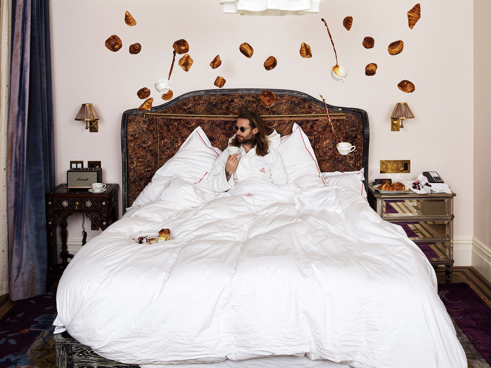Man in white robe sitting in hotel bed surrounded by floating pastries and coffee cups. Camera Hasselblad Flexbody 50 CFV ii.
"Suspended Indulgence" - The surreal intersection of comfort and fantasy in luxury accommodations