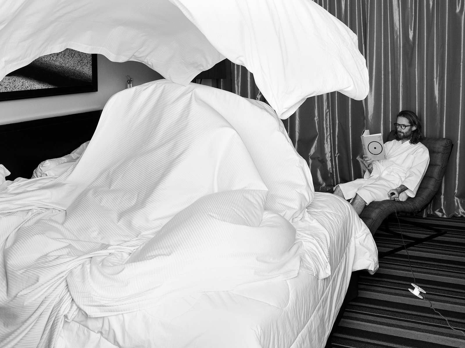 Black and white image of hotel room with dramatically billowing white bedsheets, man reading in chair. Camera Hasselblad Flexbody 50CFV ii.
"Literary Levitation" - Surreal moments of stillness amidst the ephemeral nature of hotel stays