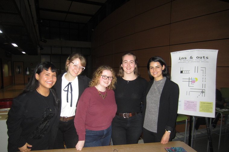 Four people smiling next to a presentation board titled: Ins and Outs