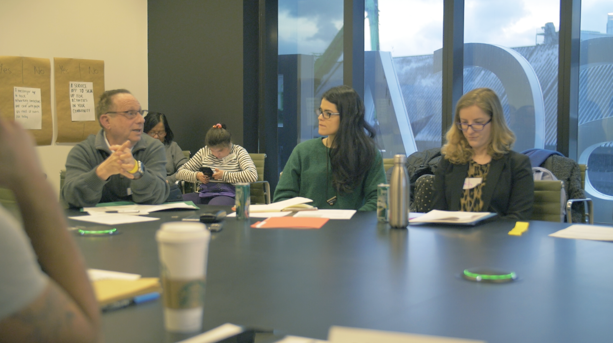A group of people listening to a person in a grey sweater and glasses. 