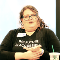 A person with curly hair, signing. They are wearing a shirt that says 'The Future is Accessible'.