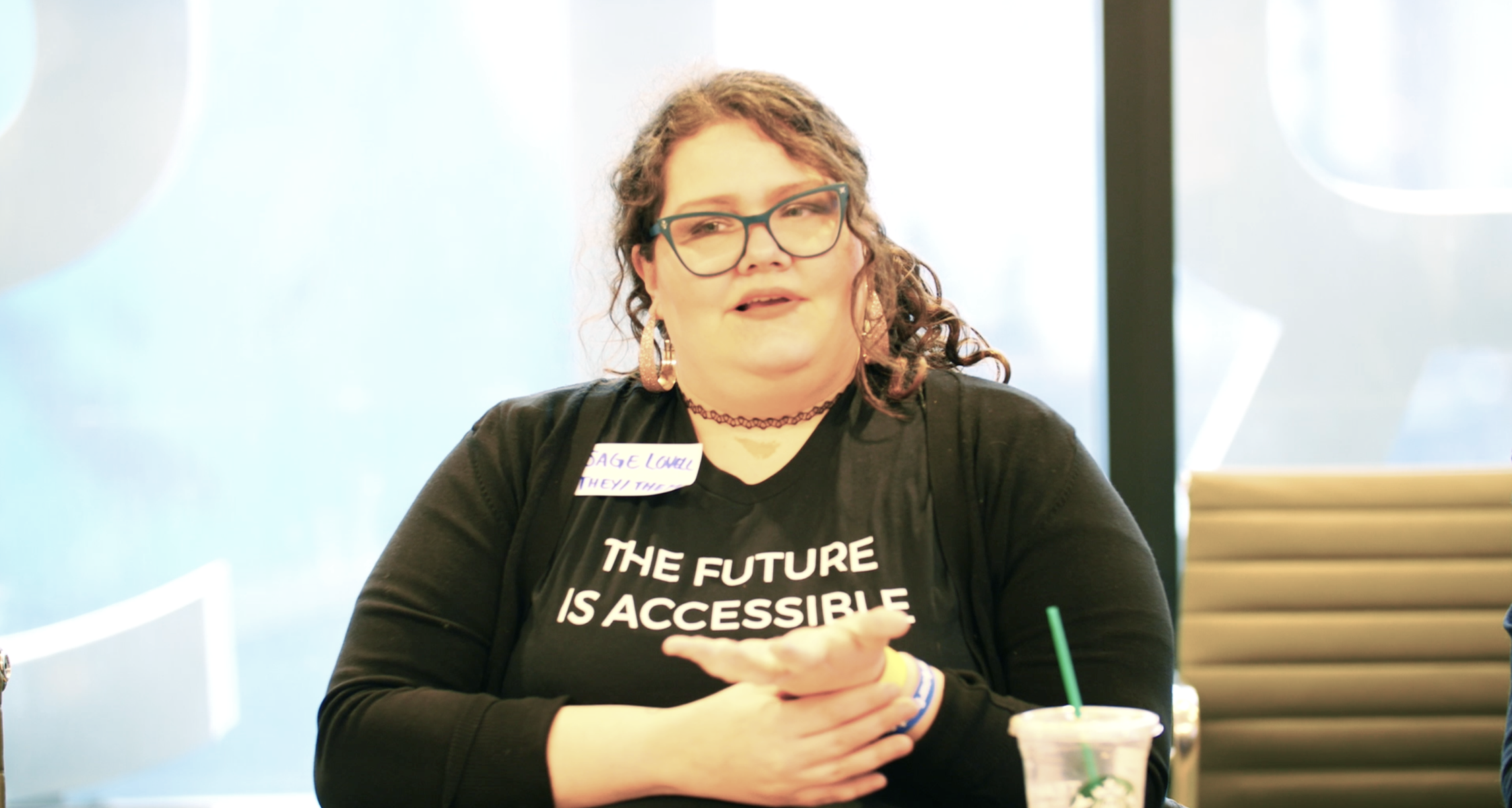 A person with curly hair, signing. They are wearing a shirt that says 'The Future is Accessible'.