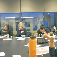 A group of people sitting at the table and one person pointing. 