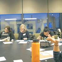 A group of people sitting at the table and one person pointing. 