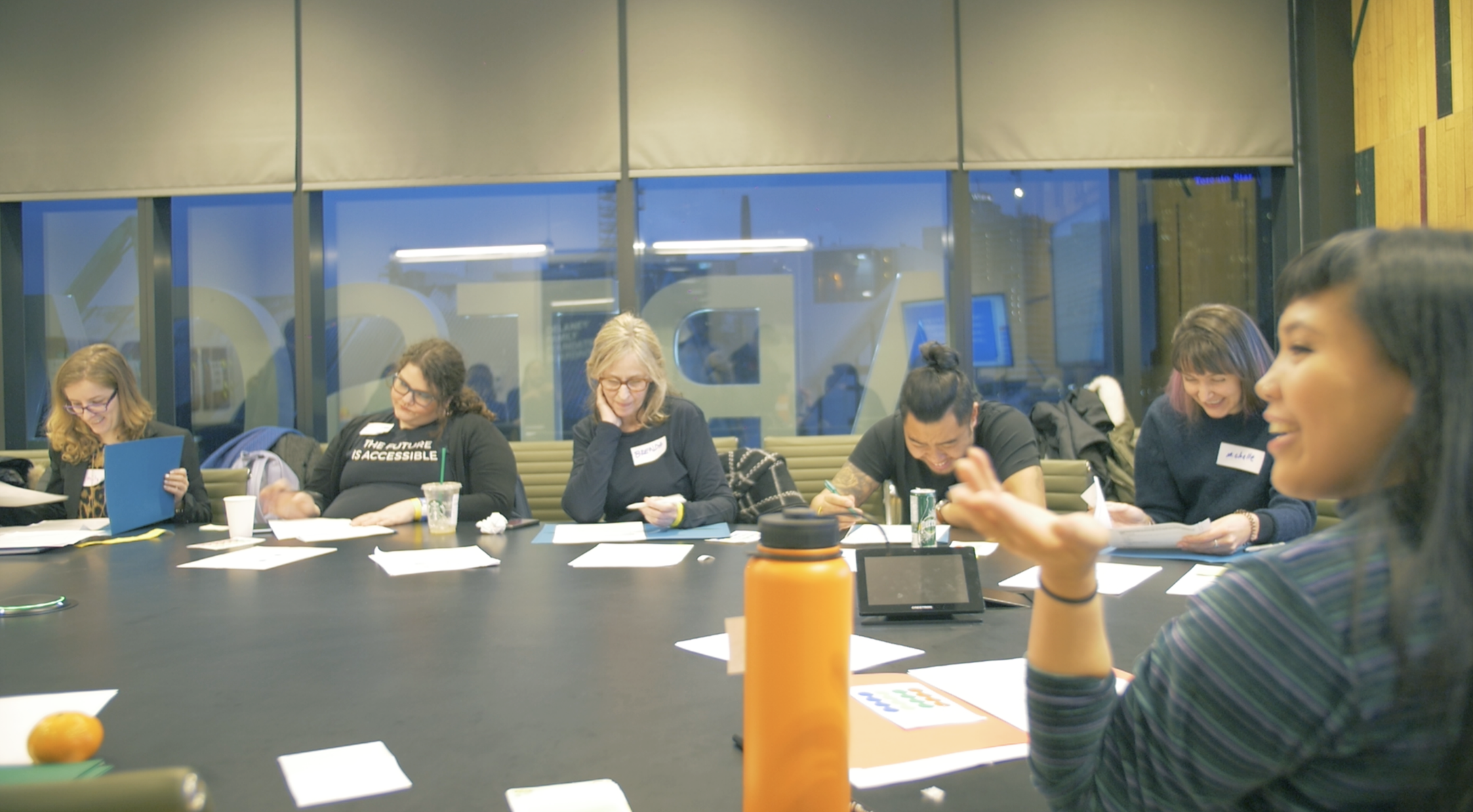 A group of people sitting at the table and one person pointing. 