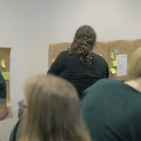 A group of people reading, writing, and placing sticky notes on the wall. 