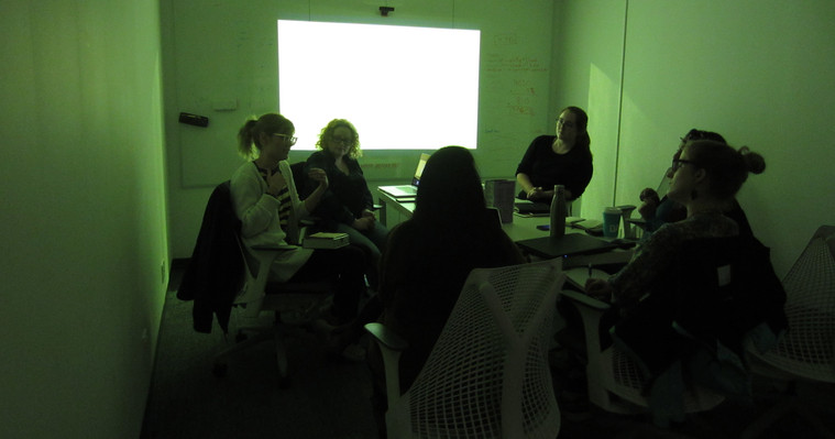 Group of students in a dark room with a powerpoint slide on.
