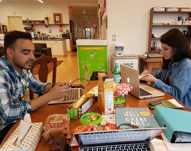 Two people working on table with food, phones, and their laptops.