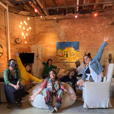 A group of people inside an industrial building, smiling, sitting on couches and raising their hands. 