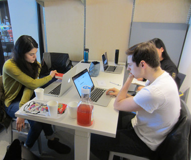 Three people sitting at a table in a room and one person is looking at a laptop screen.