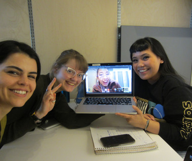 Three people smiling in a room, and one person holding a laptop with a person on a virtual call, also smiling. 