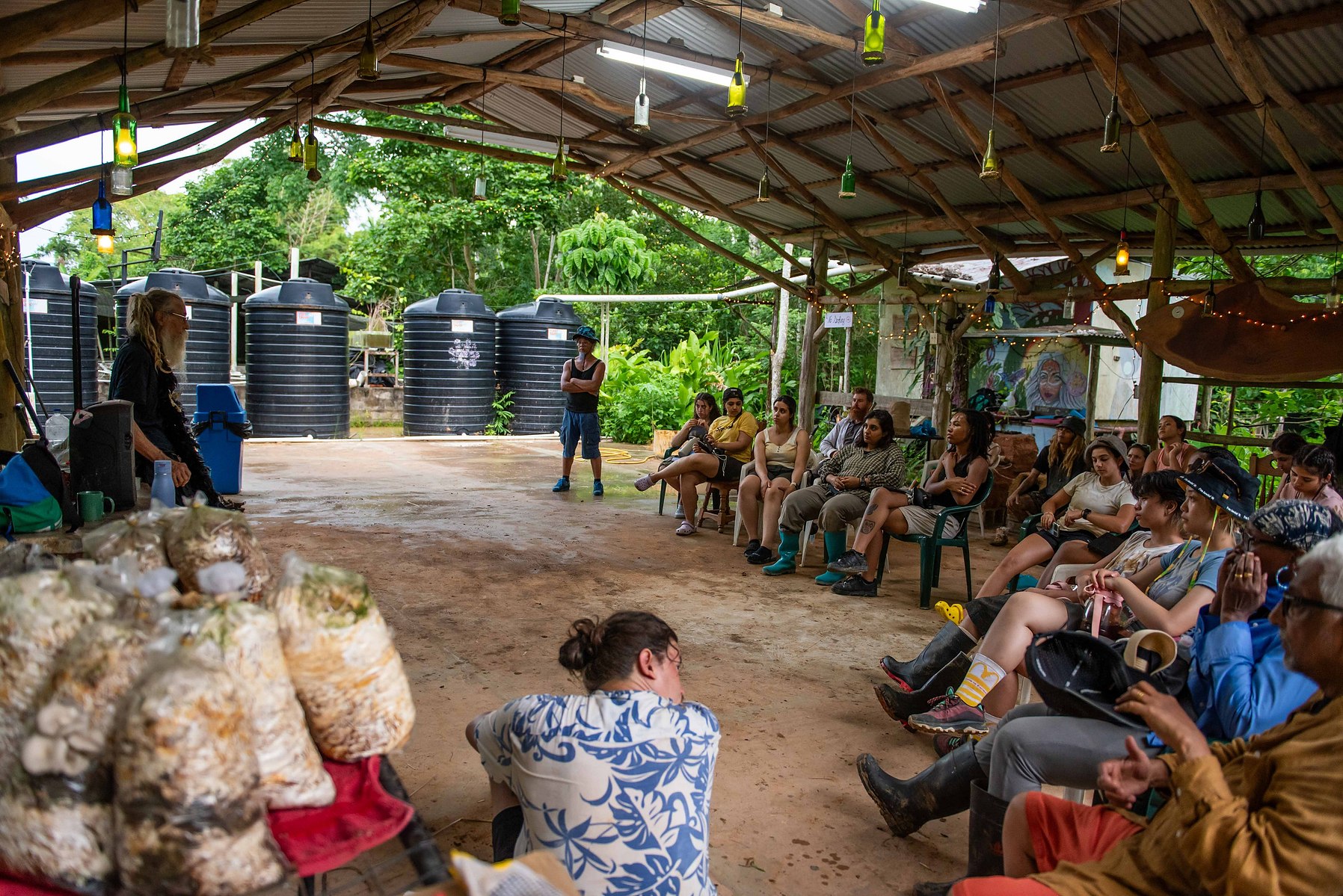 Photo of a class sitting in front of guest speaker for a university course,  Natural Building and Carnival Architectonics part of the international program at OCAD University. Taken by Leilah Dhoré at Wa Samaki Ecosystems in Freeport,Trinidad and Tobago. 