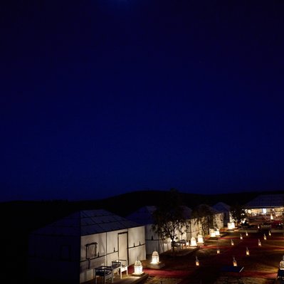 Moroccan landscape photograph featuring a desert camp at night with the moon shining near Merzouga.