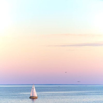 A keel sailboat coming back into harbour with a glowing pink and orange sunset over Lake Winnipeg.