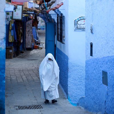 Moroccan woman wearing traditional clothing in marketplace in Chefchaouen.