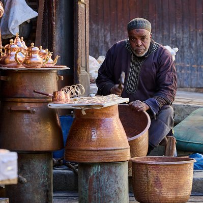 Moroccan  photograph featuring a bronze metal Souk craftsman working on a pot in Seffarine Fez. 