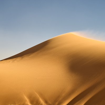 Moroccan landscape photograph featuring wind blowing off a sand dune near Merzouga.