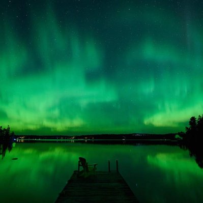 A northern lights display over a lake with a dock in the Canadian Shield portion of Canada