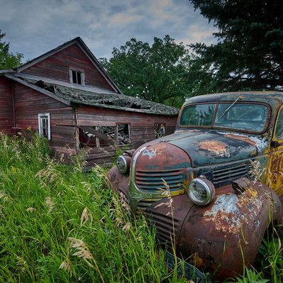 An abandoned old rusted-out old pickup truck in front of an old barn.