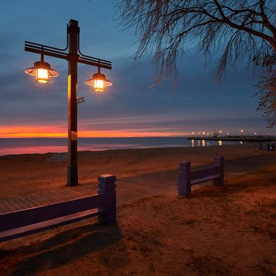 Sunrise peeking through heavy clouds over the boardwalk and lights along Lake Winnipeg.