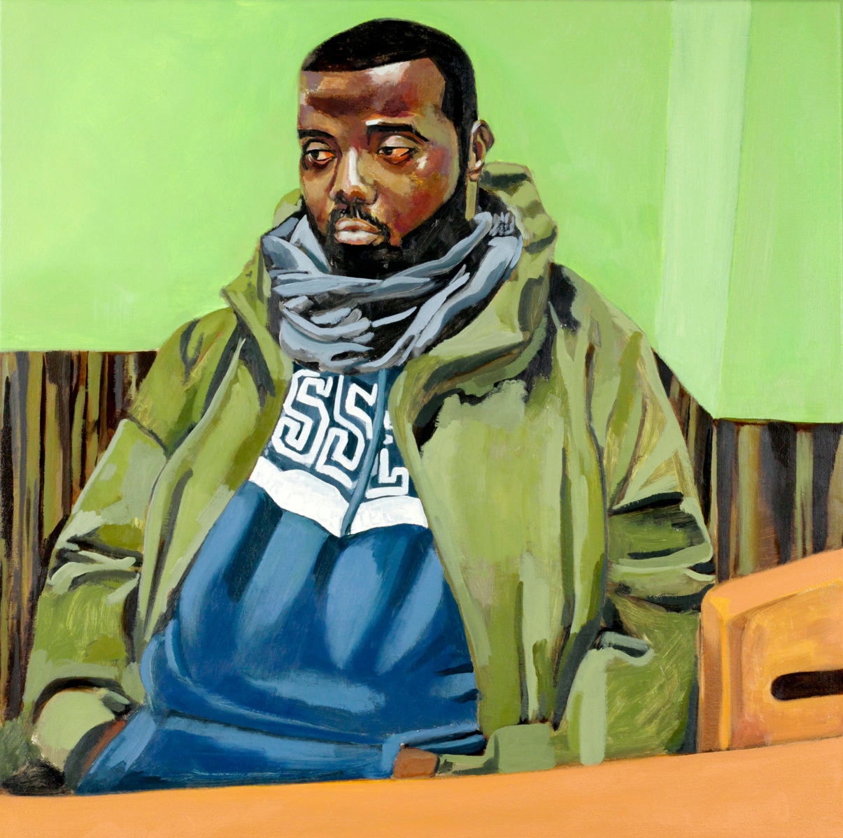 black man in olive jacket and blue hoodie for essex county college, wearing a scarf sitting at an orange table in a neon green deli.