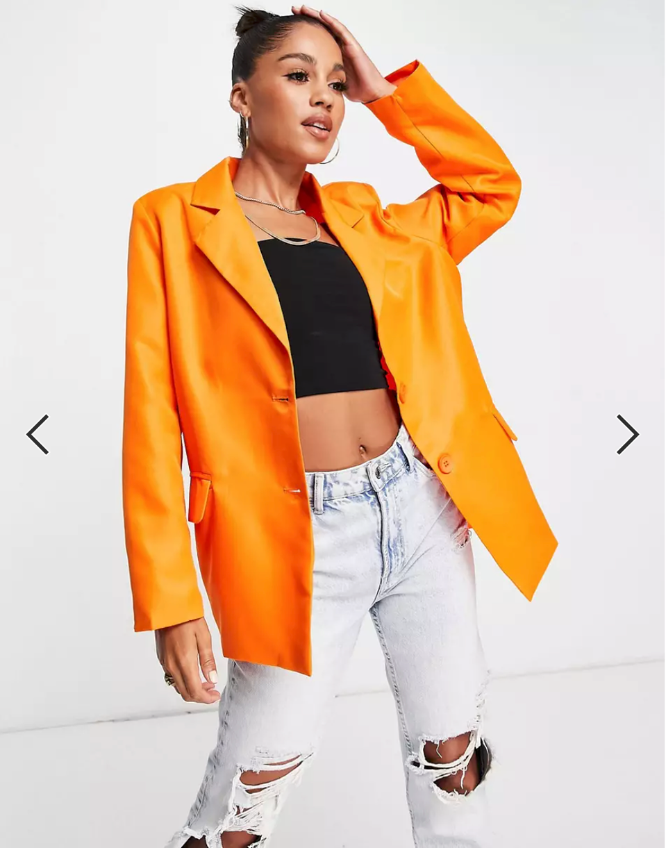 lady with one hand on her head wearing a black to with orange blazer and white ripped pants