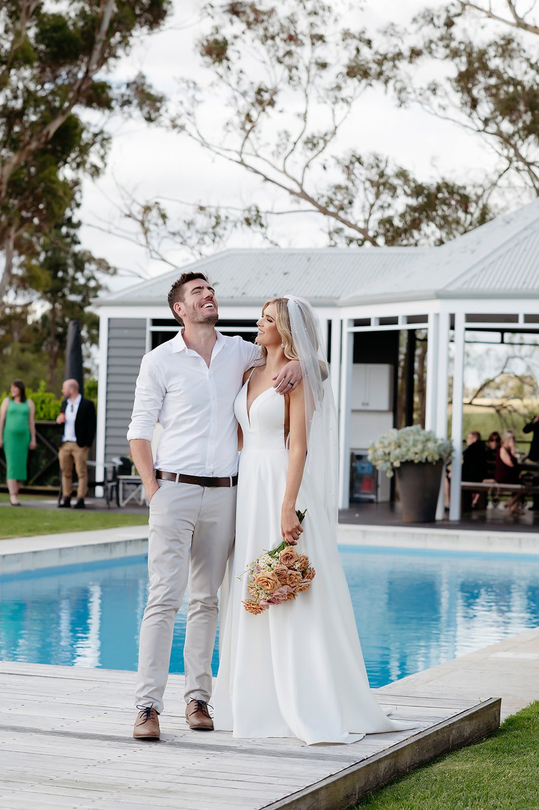 Bride and groom laughing posed in front of a pool outside