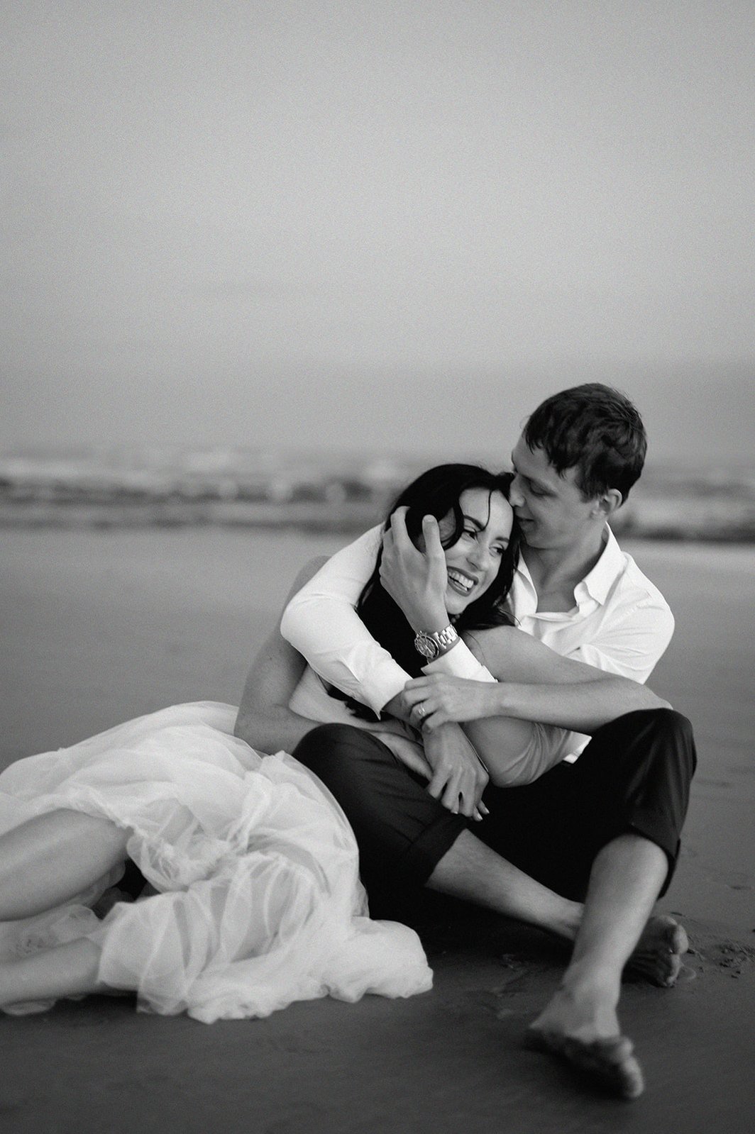 couple sitting on beach hugging 