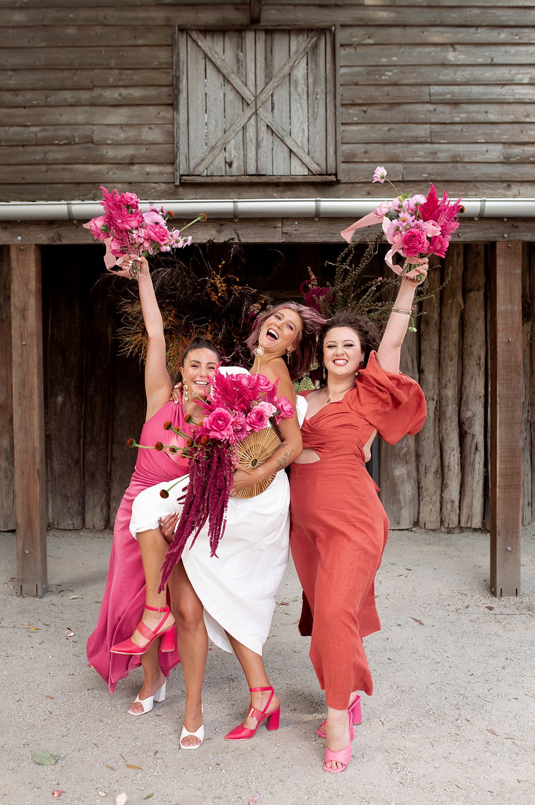bride and her two bridesmaids posing for photo smiling holding bouquets high