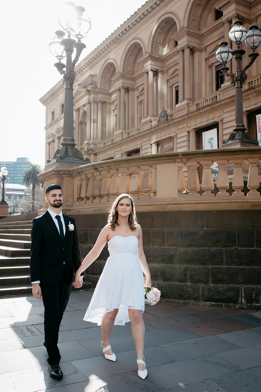 couple holding hands while walking pass a big building