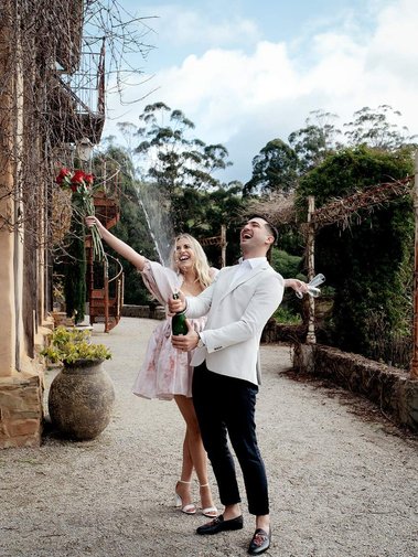 lady has arms up in air and man is popping champaign bottle in beautiful backgroud.
