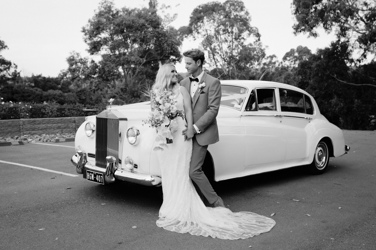 bride and groom holding each other standing in front of a car picture in black and white