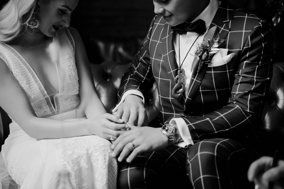 A black and white picture of a male and female couple, looking at their wedding rings on their fingers.