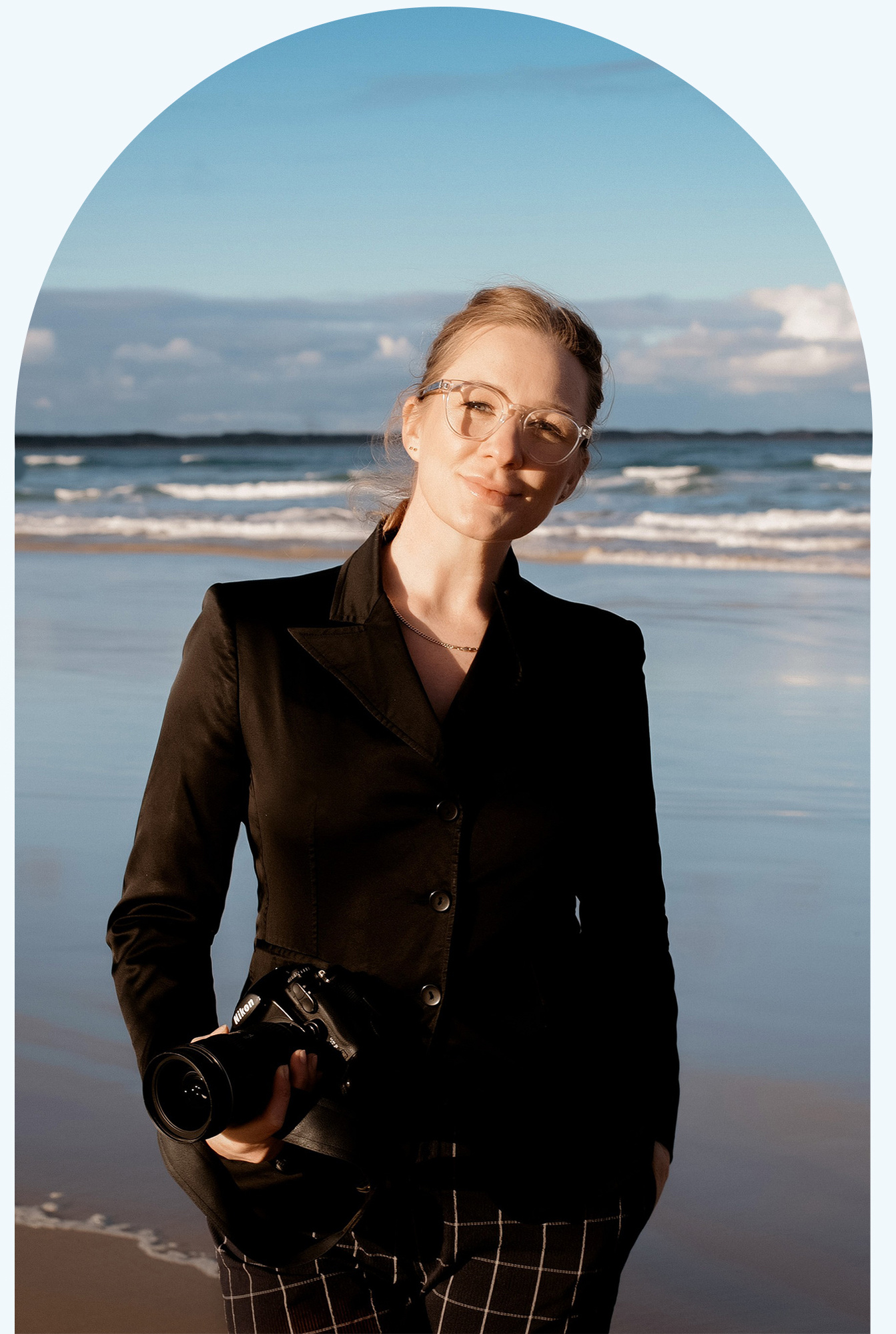 woman in a black suite wearing glasses looking at the camera on a beach