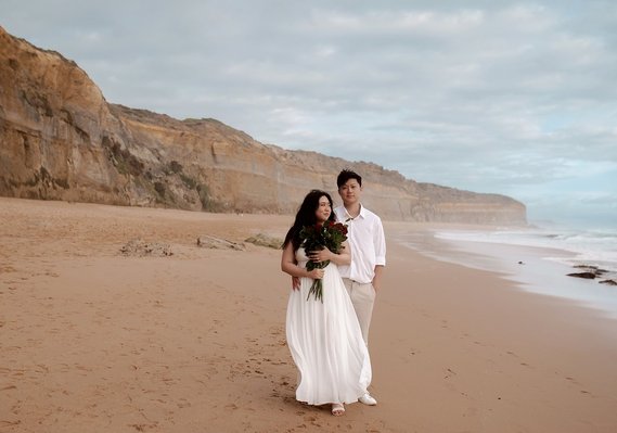 male and female posing on the great ocean road beach holding red roses.