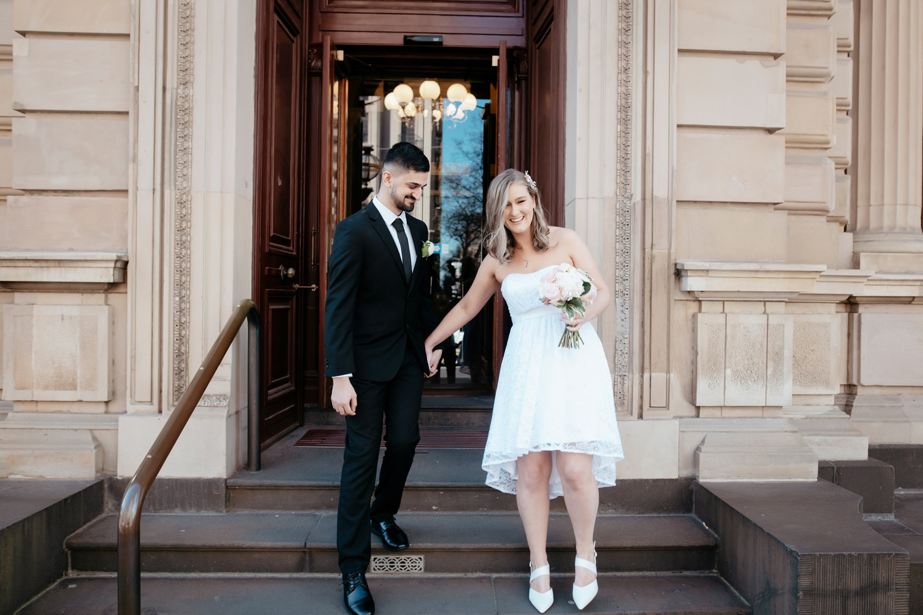 Couple standing on steps lady wearing a white dress and man in black suite