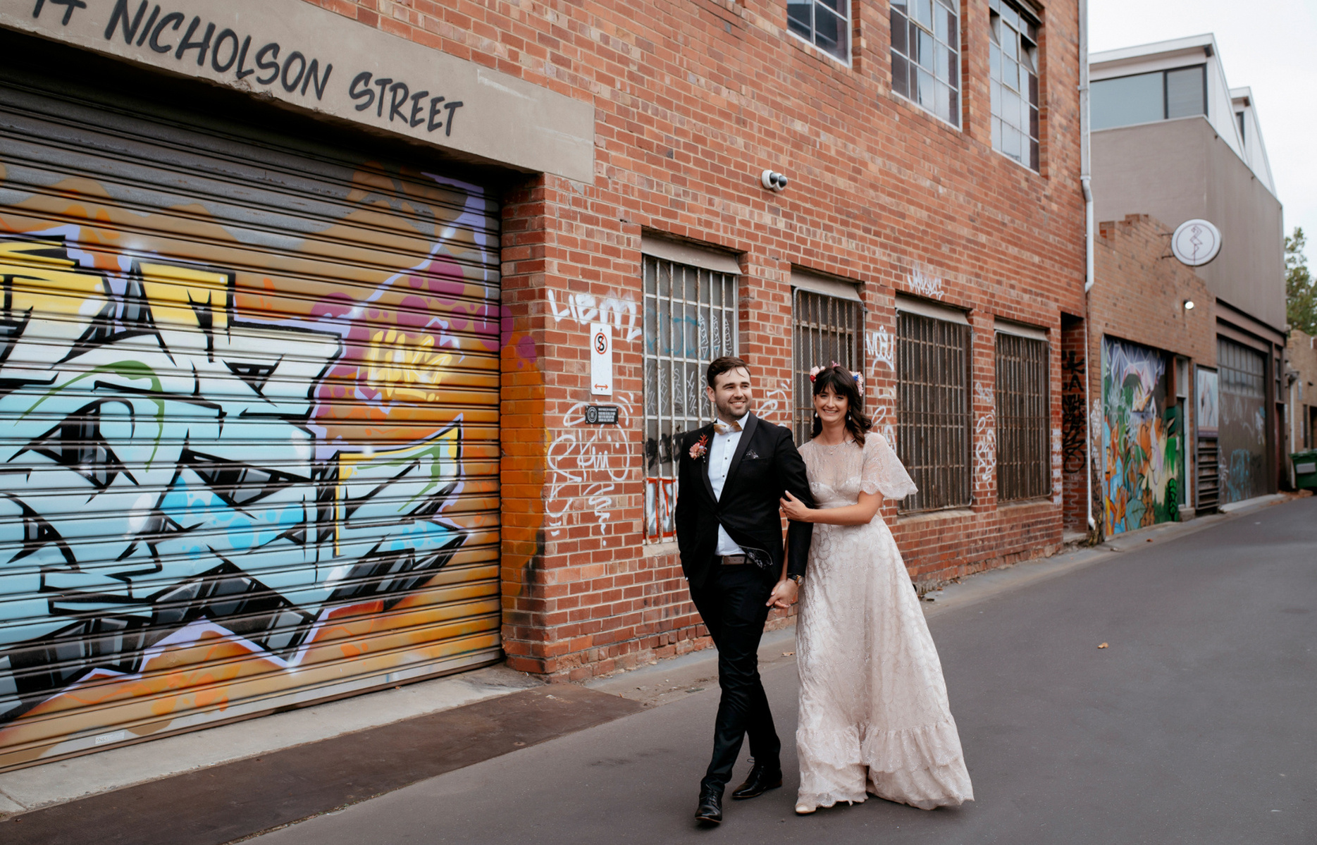 couple in arms walking pass a wall with graffiti on it 