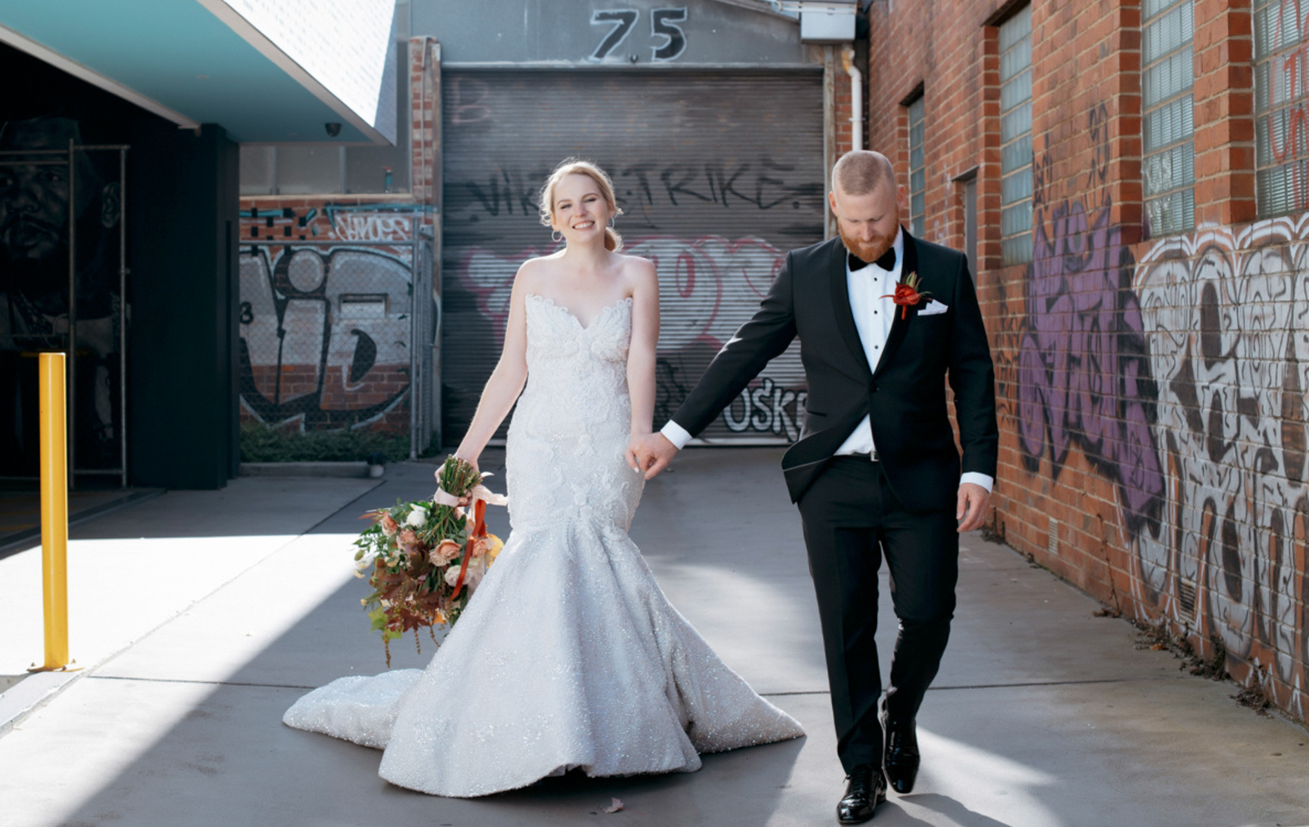 bride and groom walking with graffiti on wall next to them