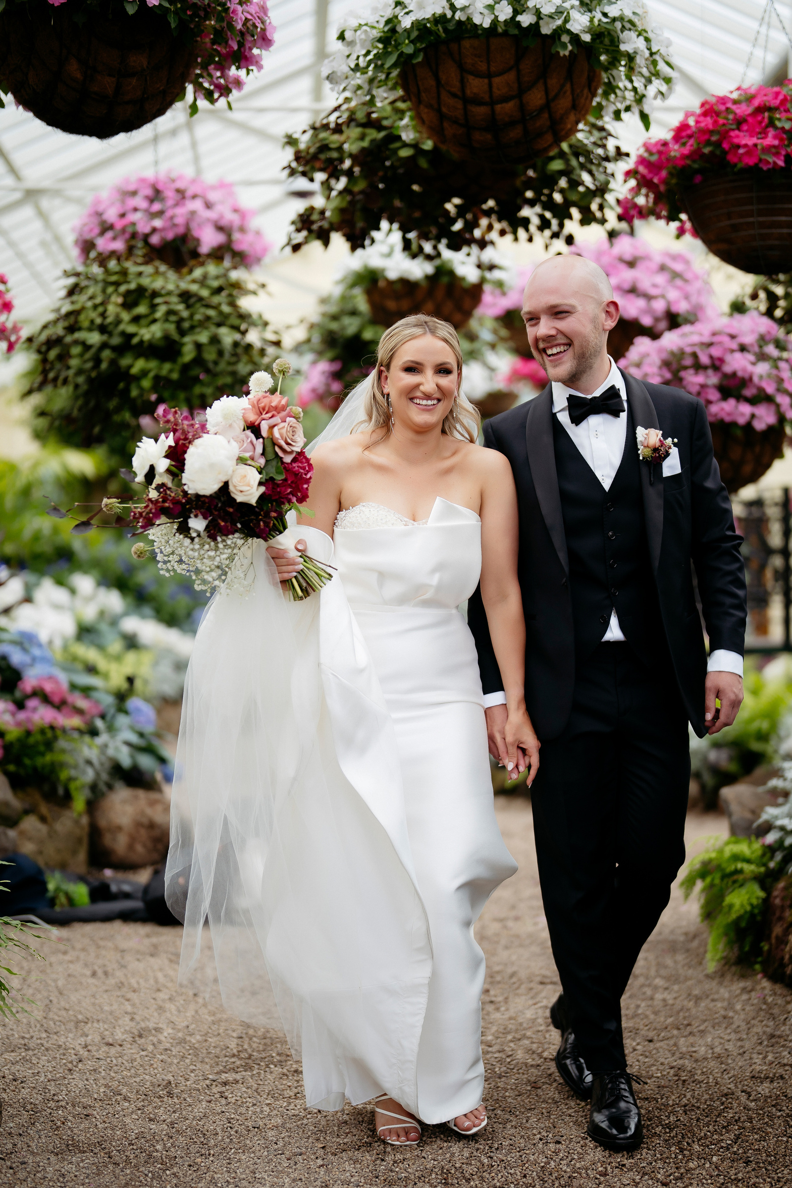 Bride and groom smiling walking through a bridge garden of flowers