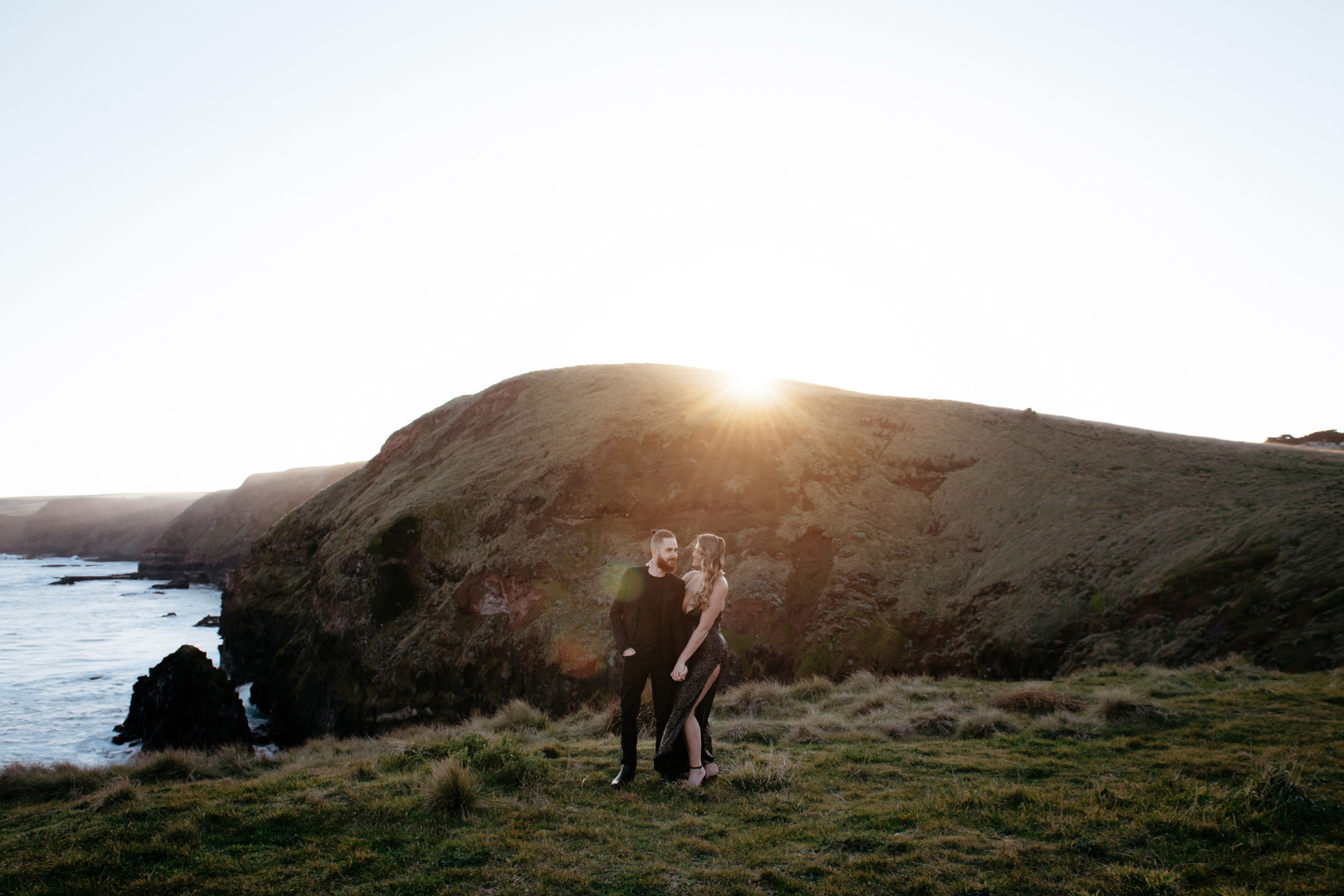 couple holding each other in a far distance with water and green hills